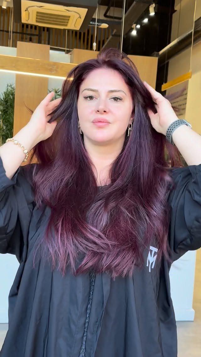 Woman showing long, wavy dark plum hair in a salon