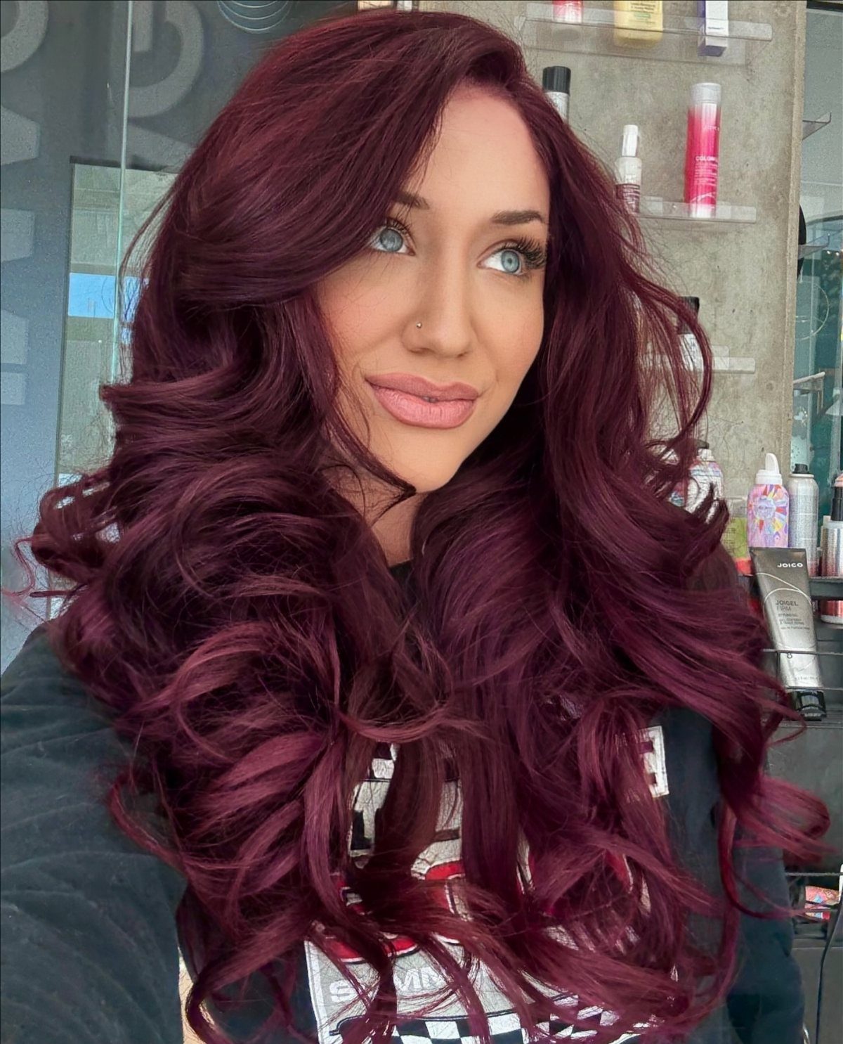 Woman with long, curled cranberry-plum hair posing in a salon