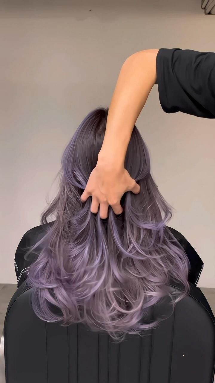 Wavy plum hair gathered by a stylist at the back of a salon chair