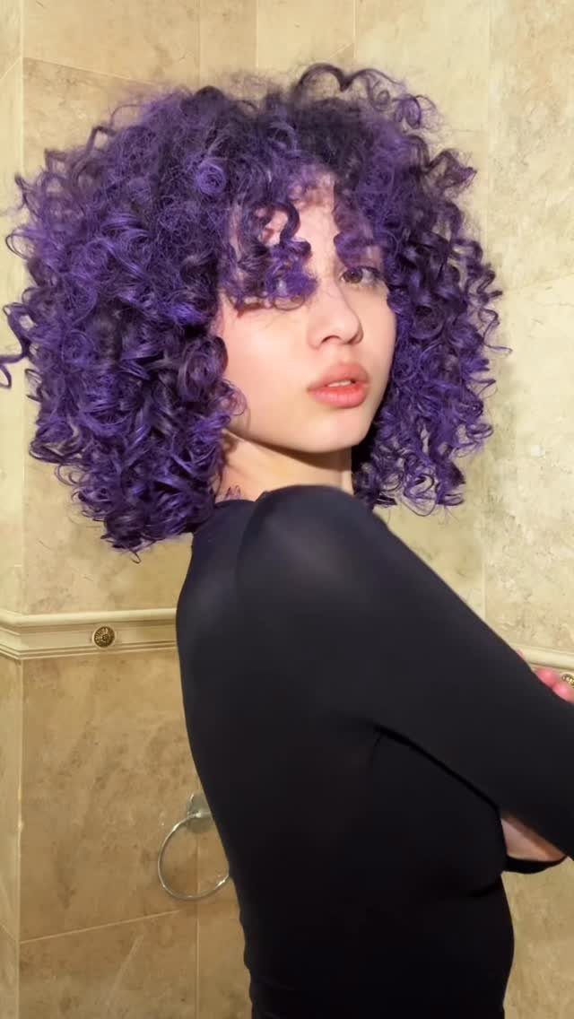 Person with vivid plum curls worn loose around the face