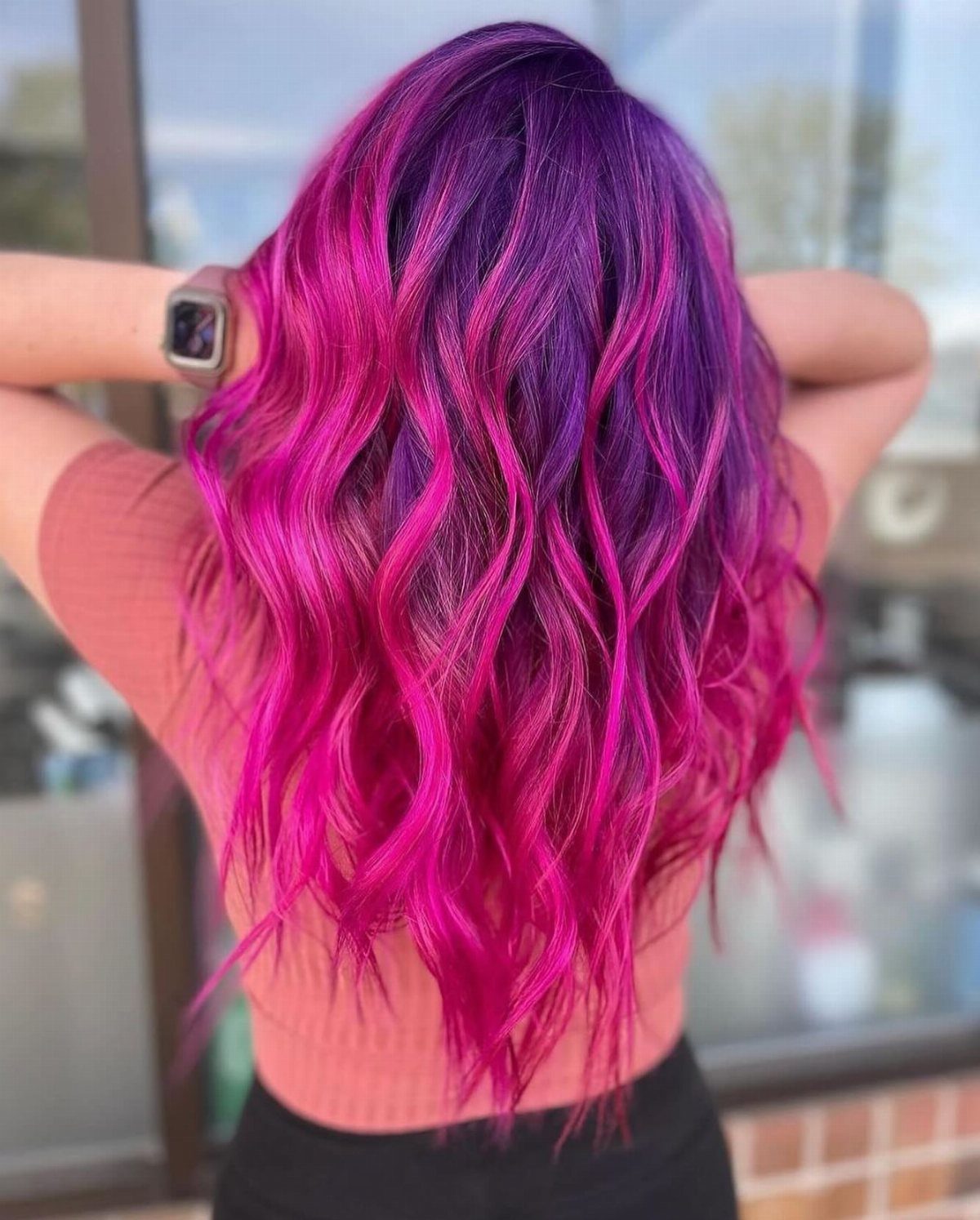 Wavy hair blends deep plum roots into vivid magenta-pink ends