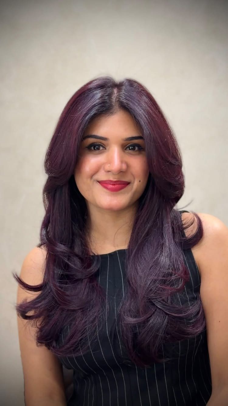 Woman posing with long, layered violet-plum hair against a light wall