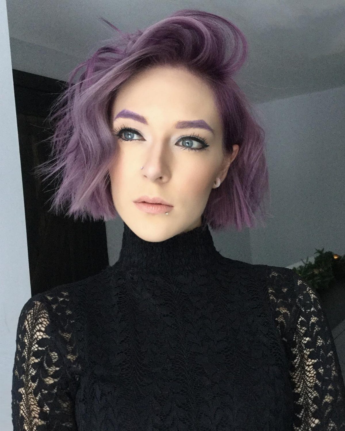 Person with a tousled dusty mauve bob wearing a black lace top