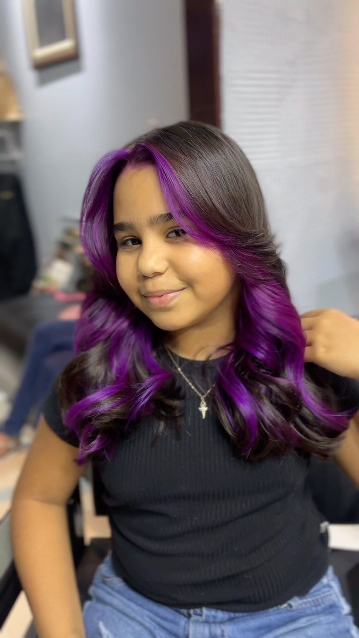 Young woman with dark roots and vivid purple curls posing in a salon.