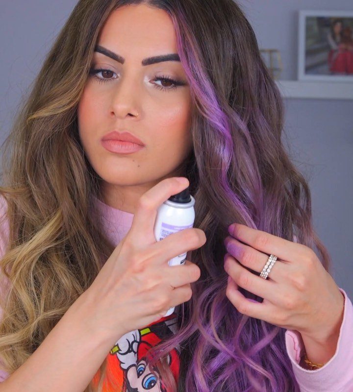 Woman sprays purple color onto long brown hair, creating vivid purple strands.