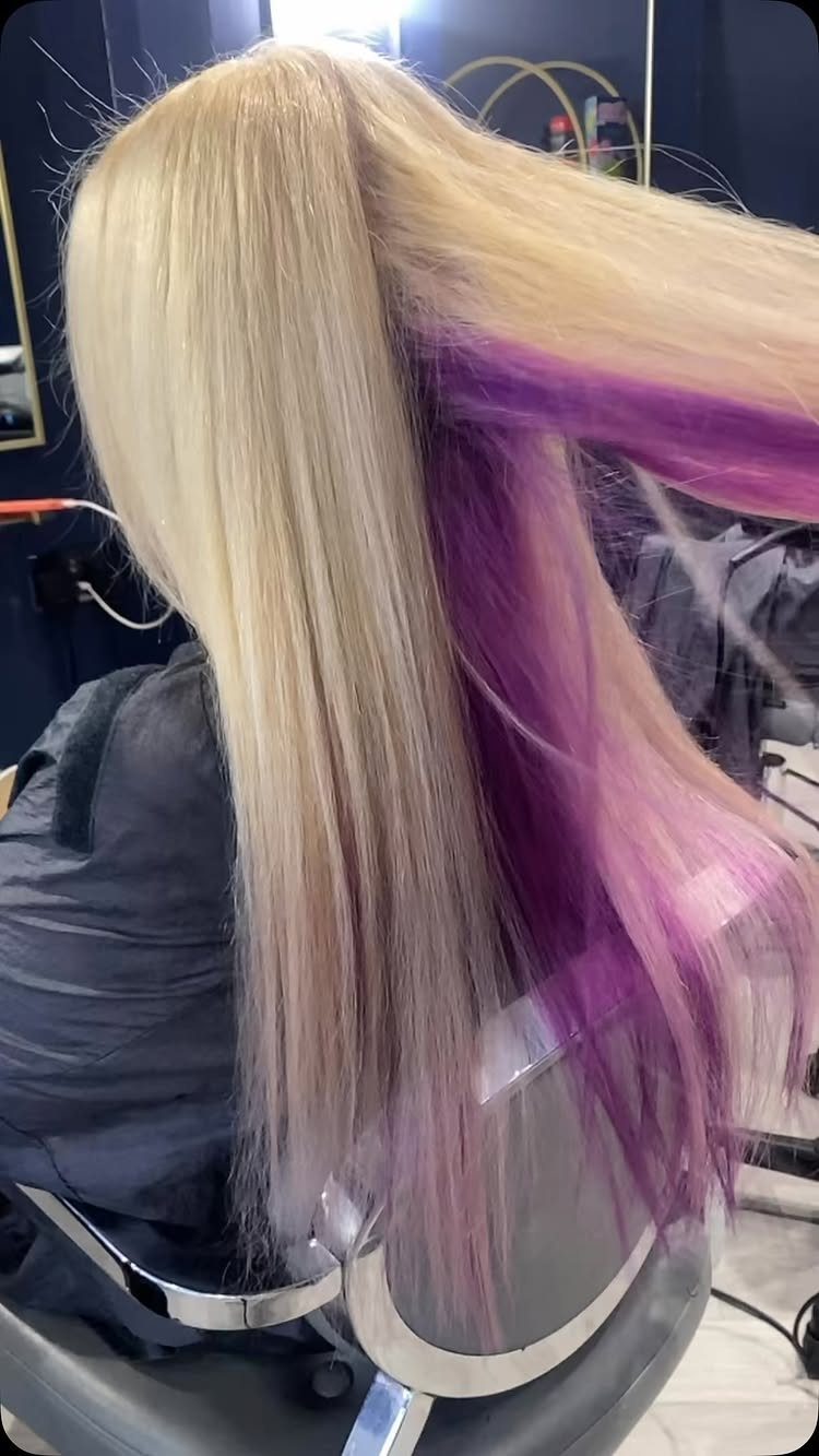 Blonde hair lifted to reveal vivid purple and pink underneath layers in a salon.