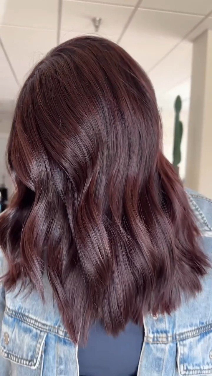 Glossy burgundy hair falls over a light blue denim jacket