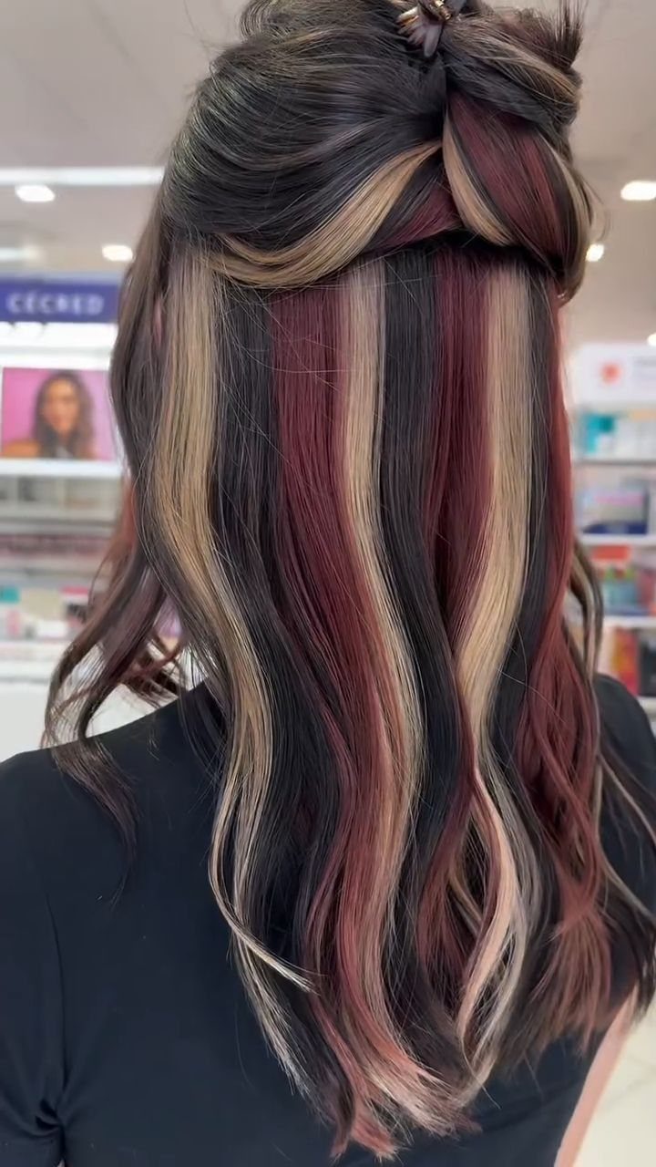 Long dark hair with thick blonde and burgundy highlights in a salon