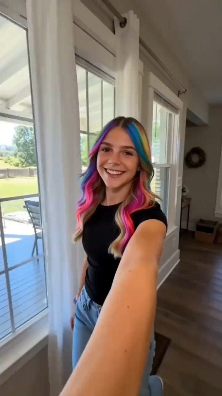 Woman with long, brightly colored blue, pink, purple, and orange hair smiling indoors