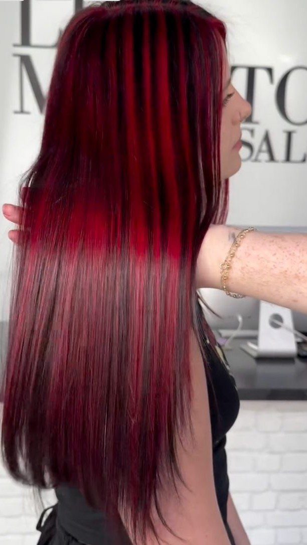 Long straight dark hair with vivid red streaks displayed against a salon background