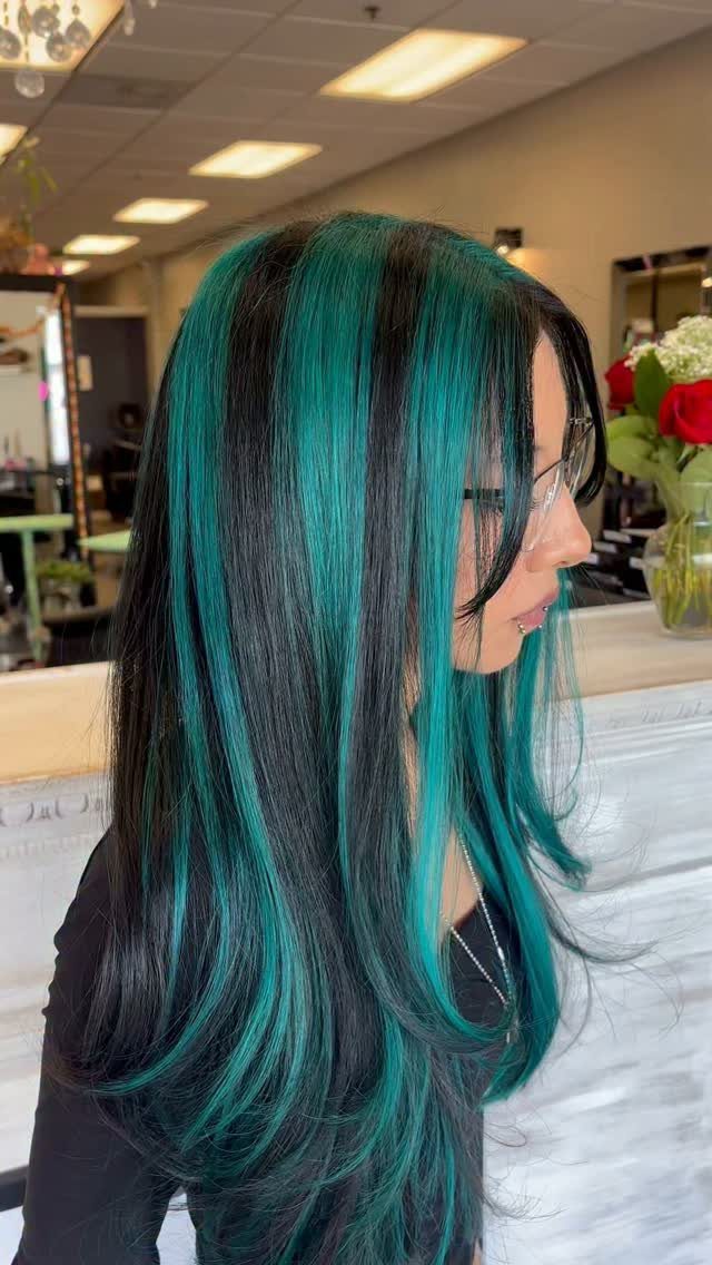Long dark hair with vivid teal highlights styled in a salon