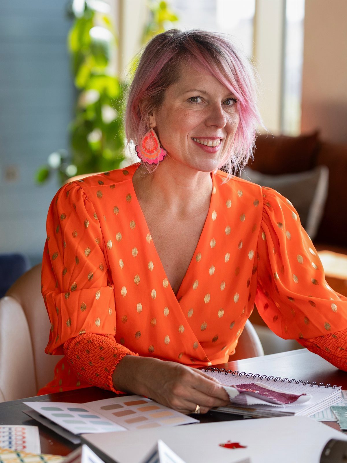 Woman with short dusty rose hair seated beside color swatches and an open notebook