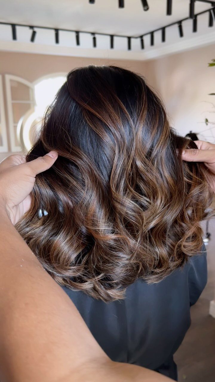 Dark brown curls with soft caramel balayage highlights shown from behind