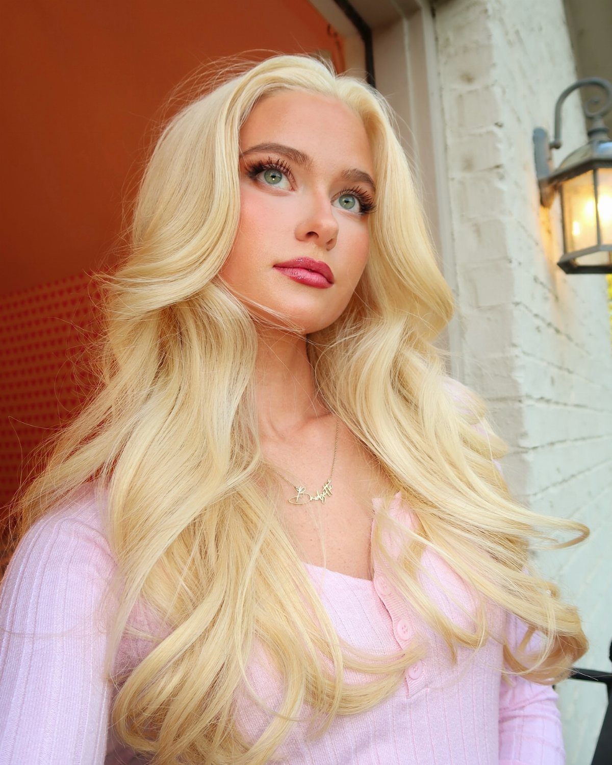 Woman with long pale blonde hair posing beside an orange and white wall