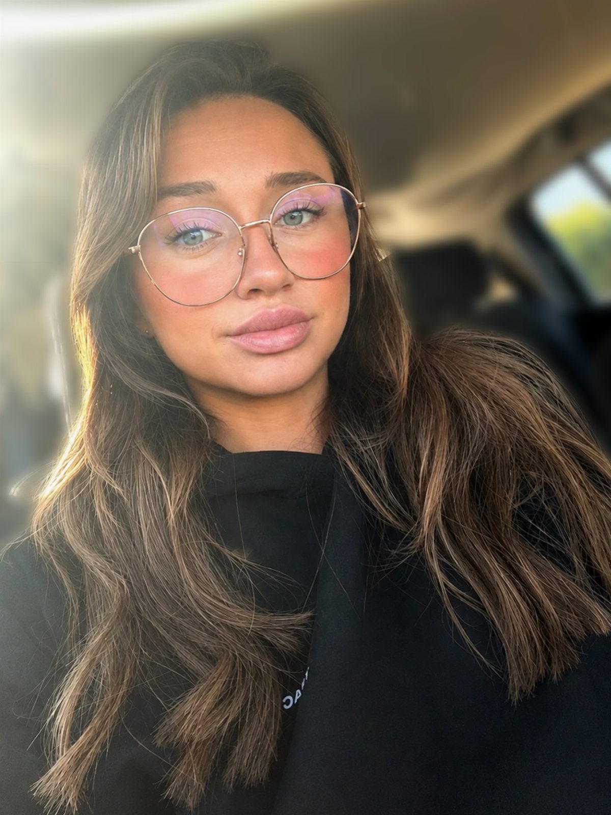 Woman with long warm brown hair and lighter strands wearing round glasses