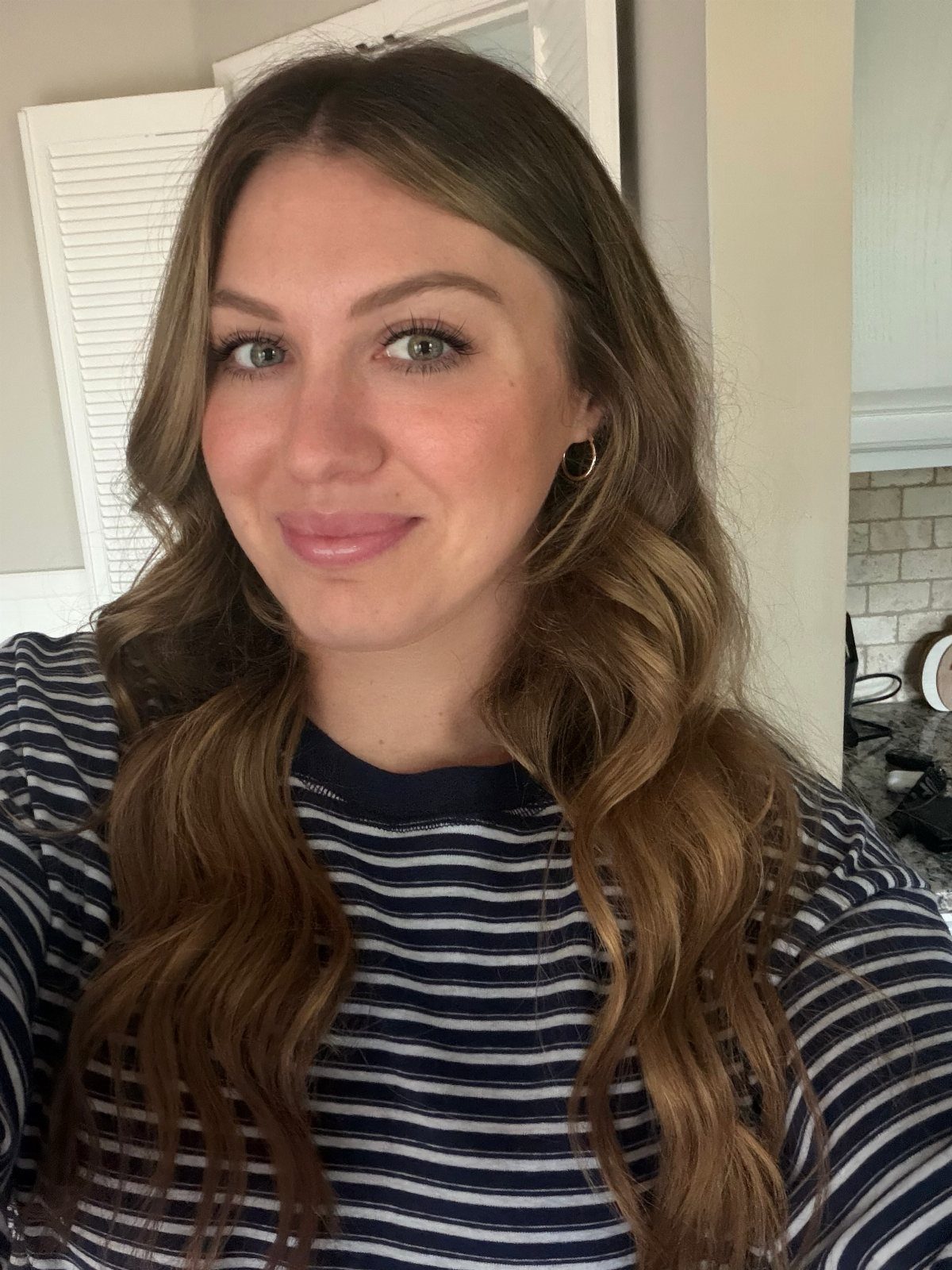 Woman posing with long, wavy medium brown hair and a striped shirt