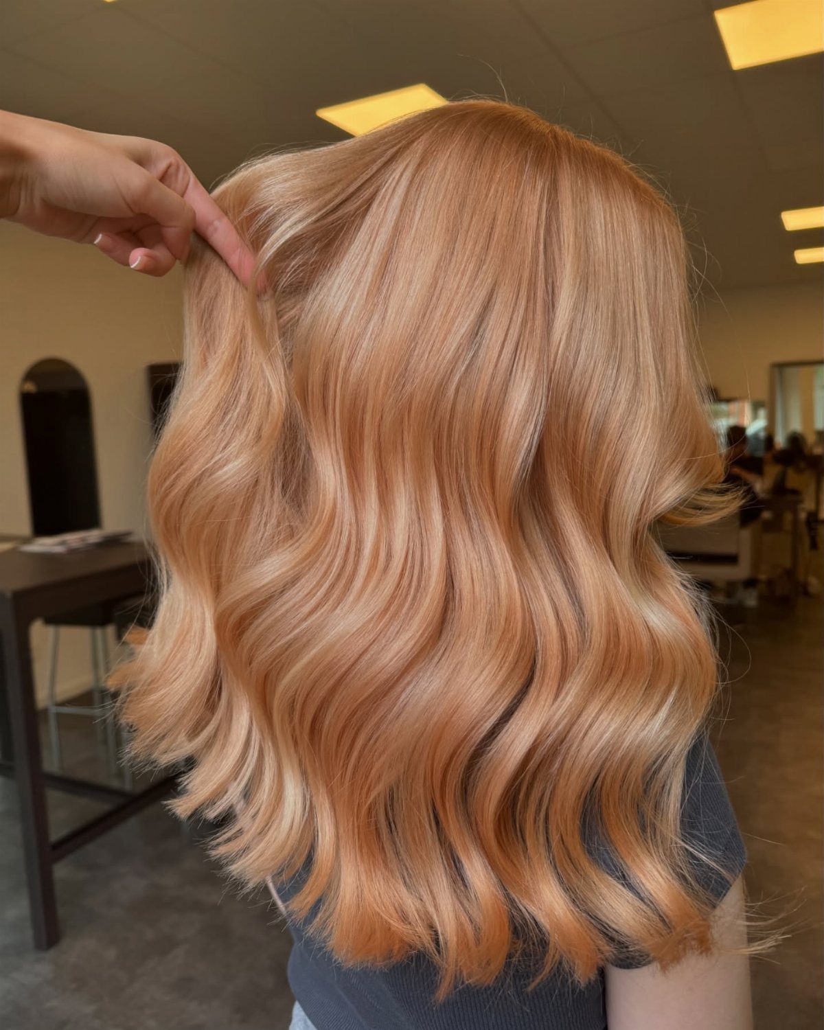 Wavy strawberry blonde hair with a salon stylist pointing to a section