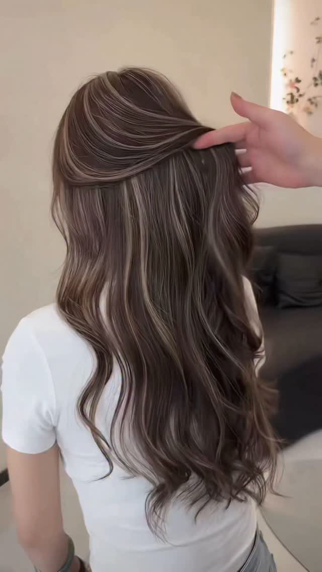 Long dark brown hair with fine pale balayage highlights lifted by a hand