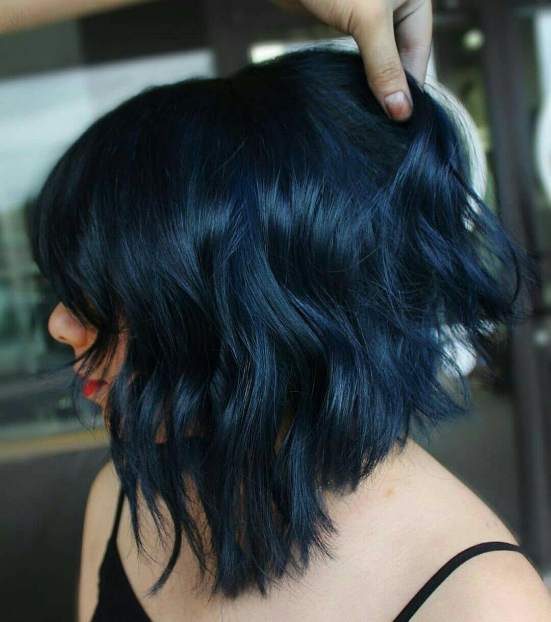 Layered blue-black hair with navy highlights lifted by a hand