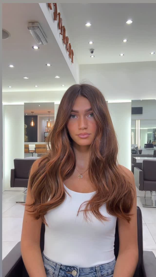 Woman with long, softly highlighted brown hair seated in a bright salon