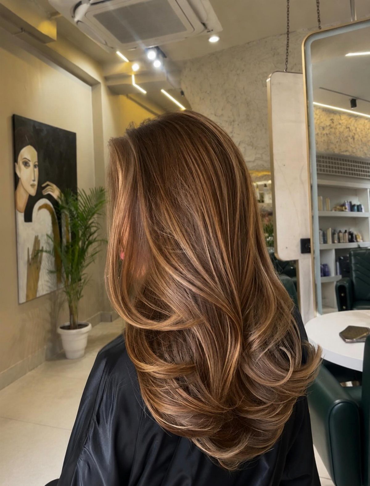 Layered brown hair with caramel-blonde highlights and softly curled ends
