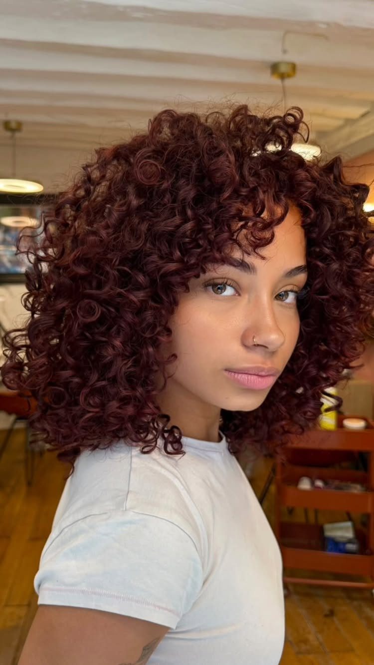 Woman displaying voluminous dark reddish-brown curls with subtle violet tones
