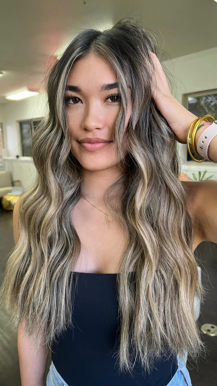 Woman with long wavy brown hair and delicate blonde highlights throughout