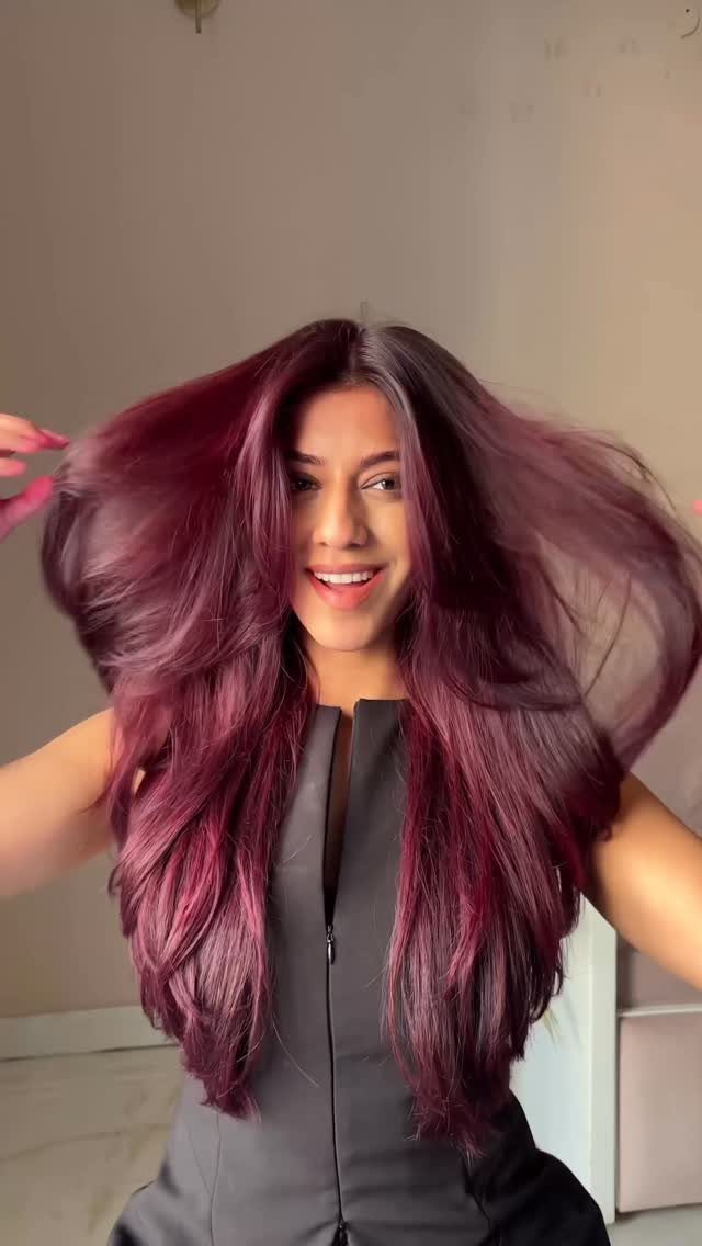 Woman showing long, voluminous dark magenta hair with vivid pink and purple tones