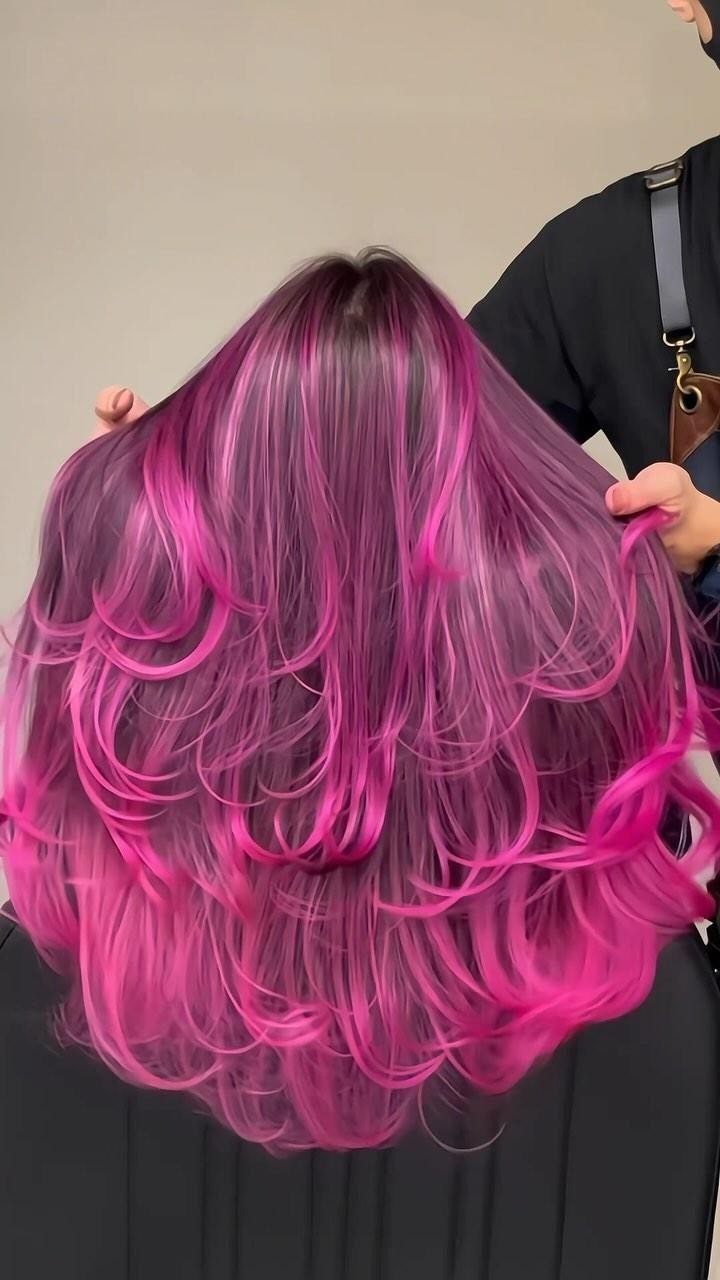 Vivid neon pink layered hair with darker roots and curled ends
