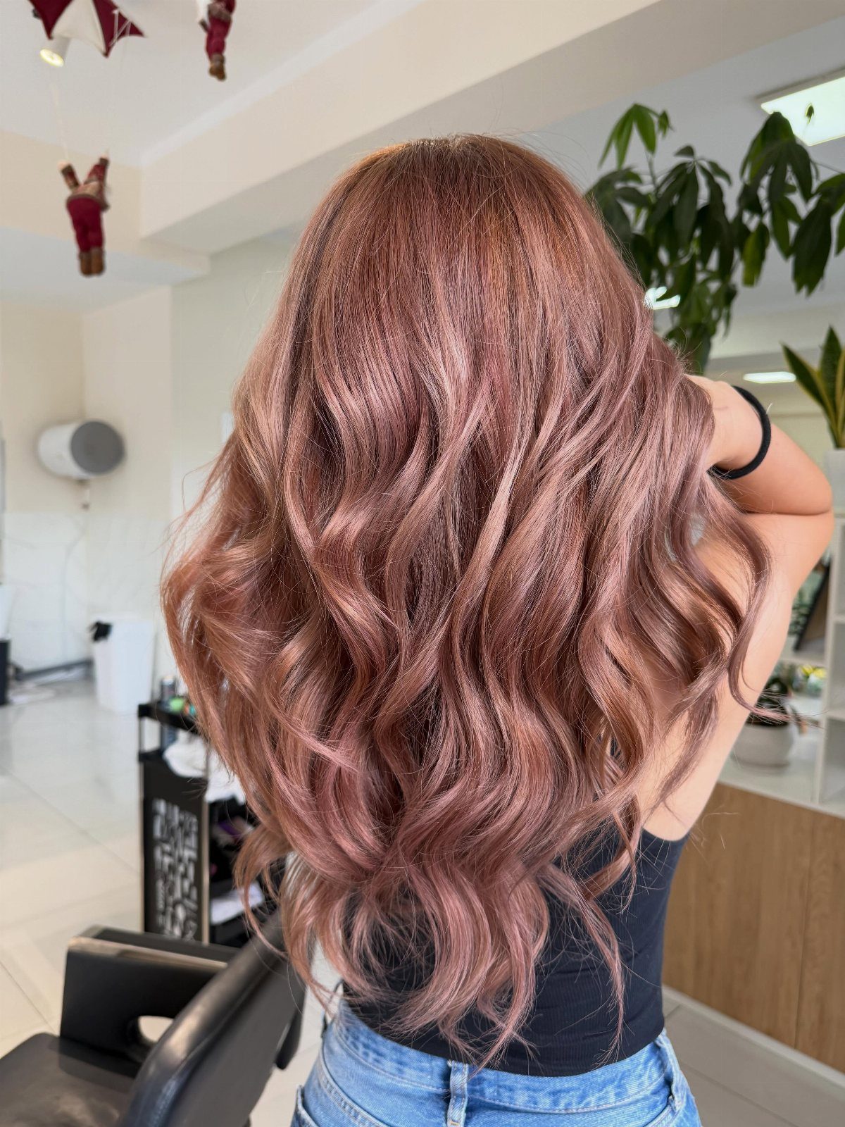 Long wavy dusty rose-pink hair shown from behind in a salon