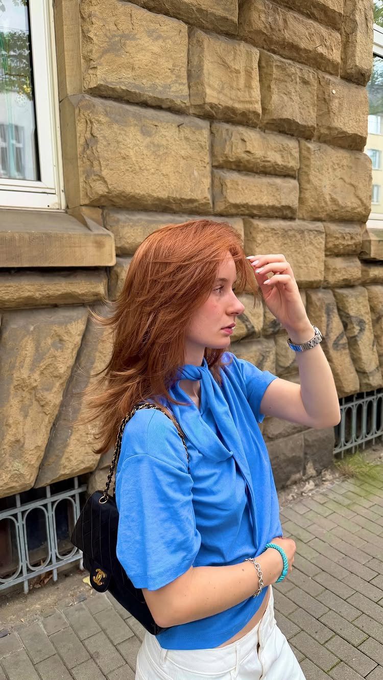 Woman with long copper-red hair standing beside a tan stone wall