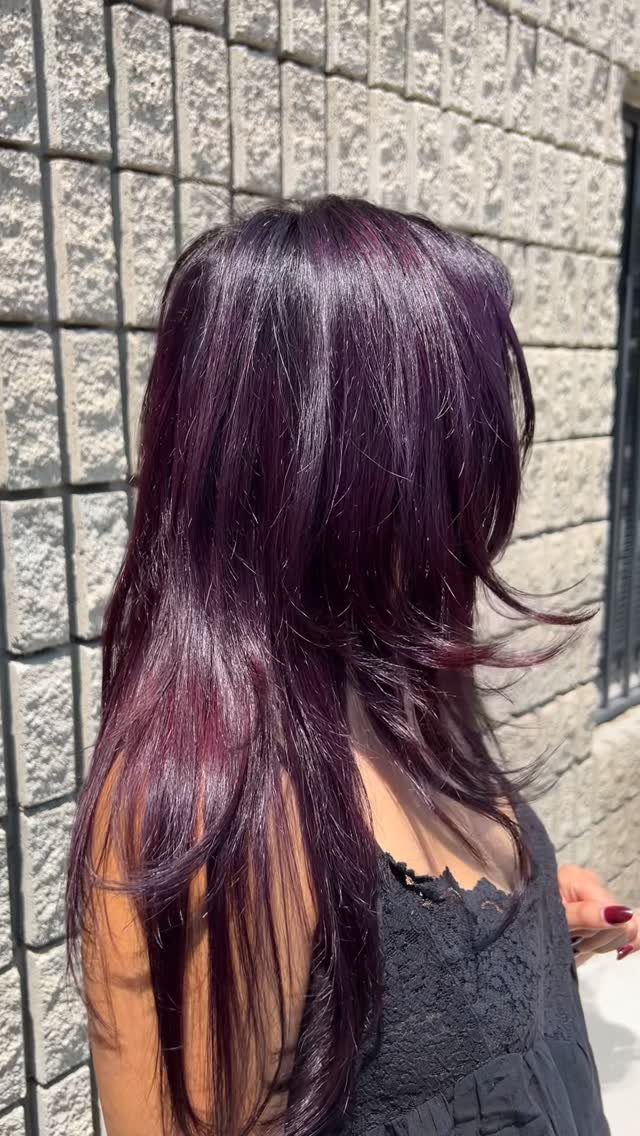 Long glossy deep violet hair with lighter purple strands against a gray stone wall