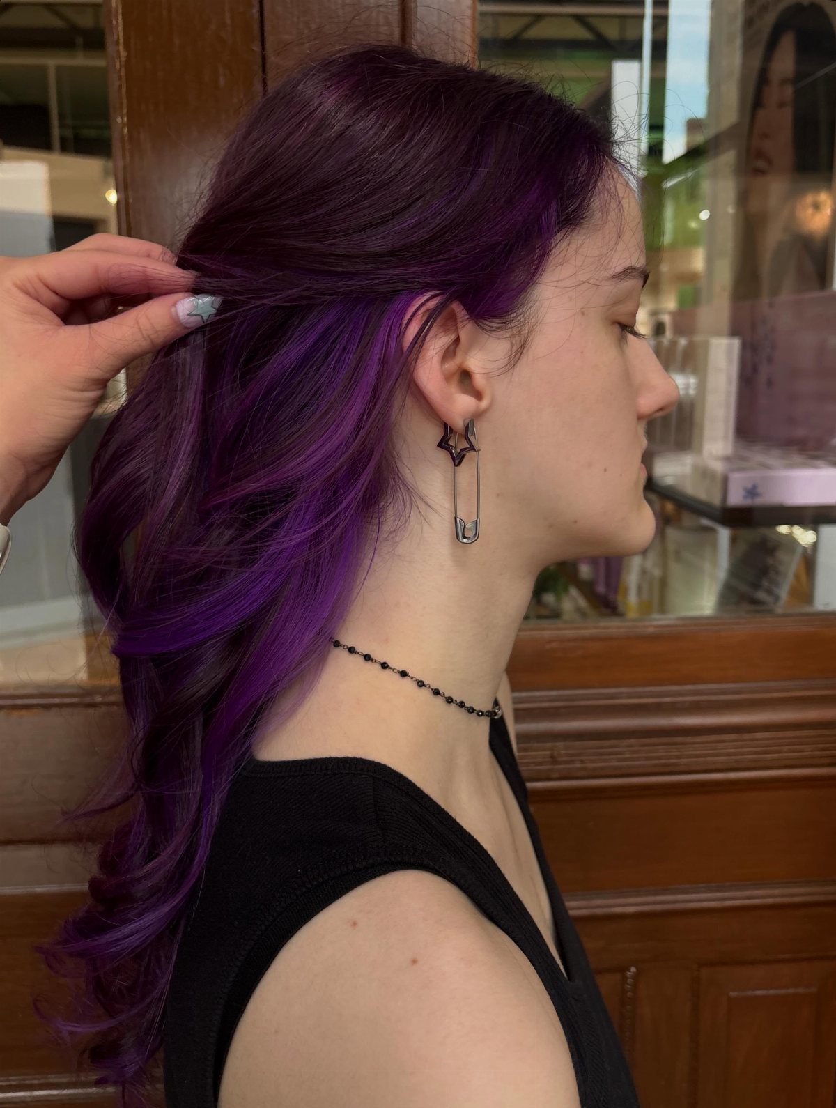 Purple sections show beneath dark curled hair as a hand lifts a layer