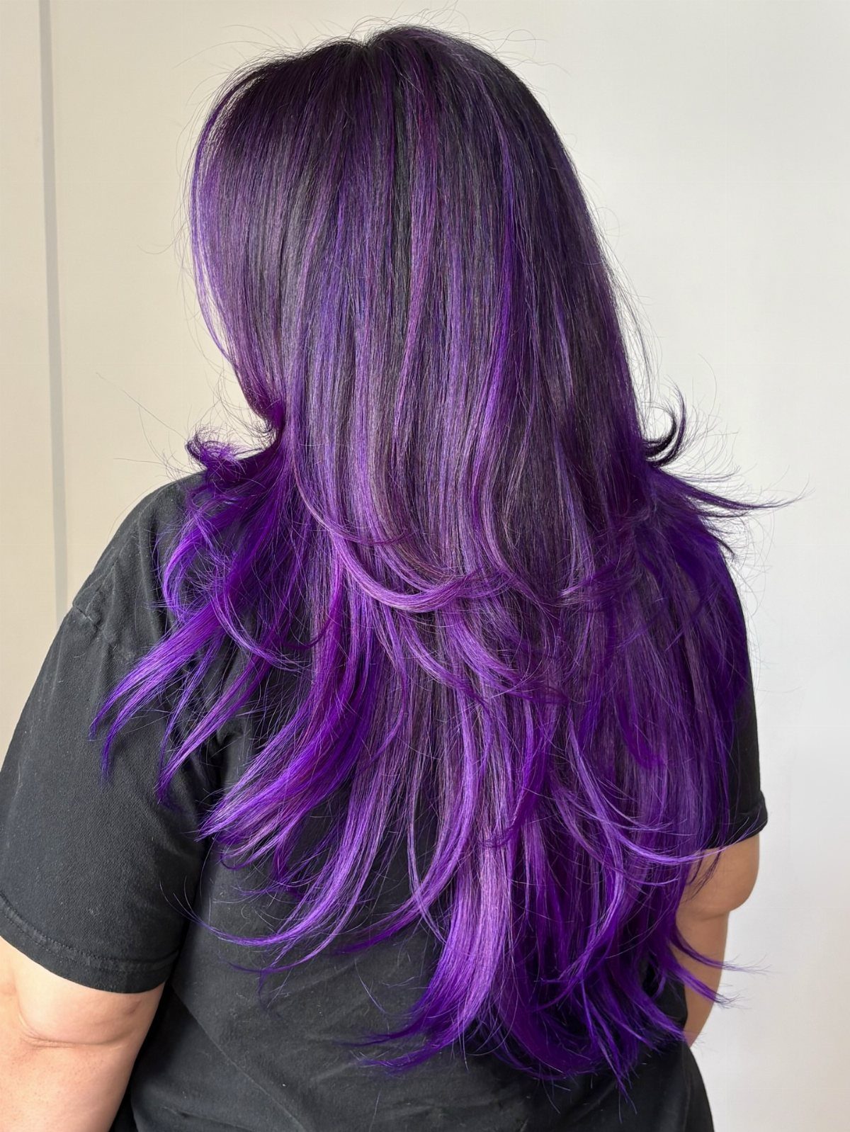 Long layered hair shows dark roots and upper layers with vivid purple lengths