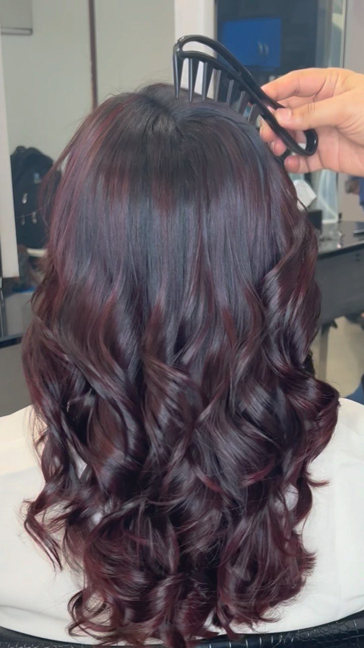 Long burgundy-purple hair styled in glossy curls at a salon
