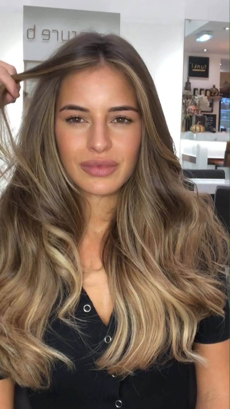 Woman with long brown waves and bright blonde face-framing highlights in a salon