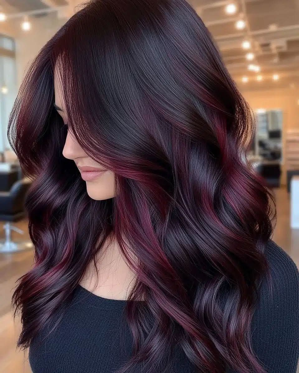 Long dark waves feature deep burgundy face-framing highlights in a bright salon