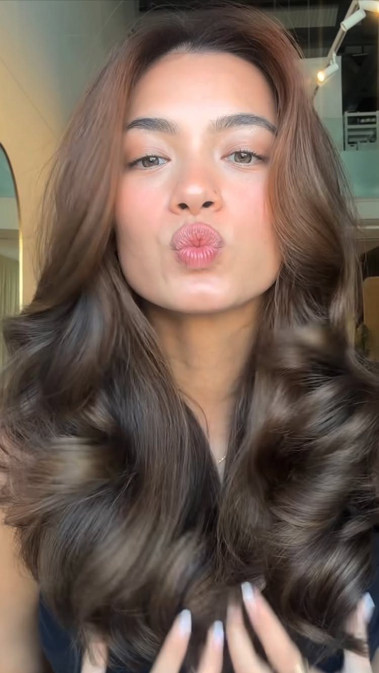 Woman showing long dark brunette hair with subtle warm caramel highlights and voluminous curls