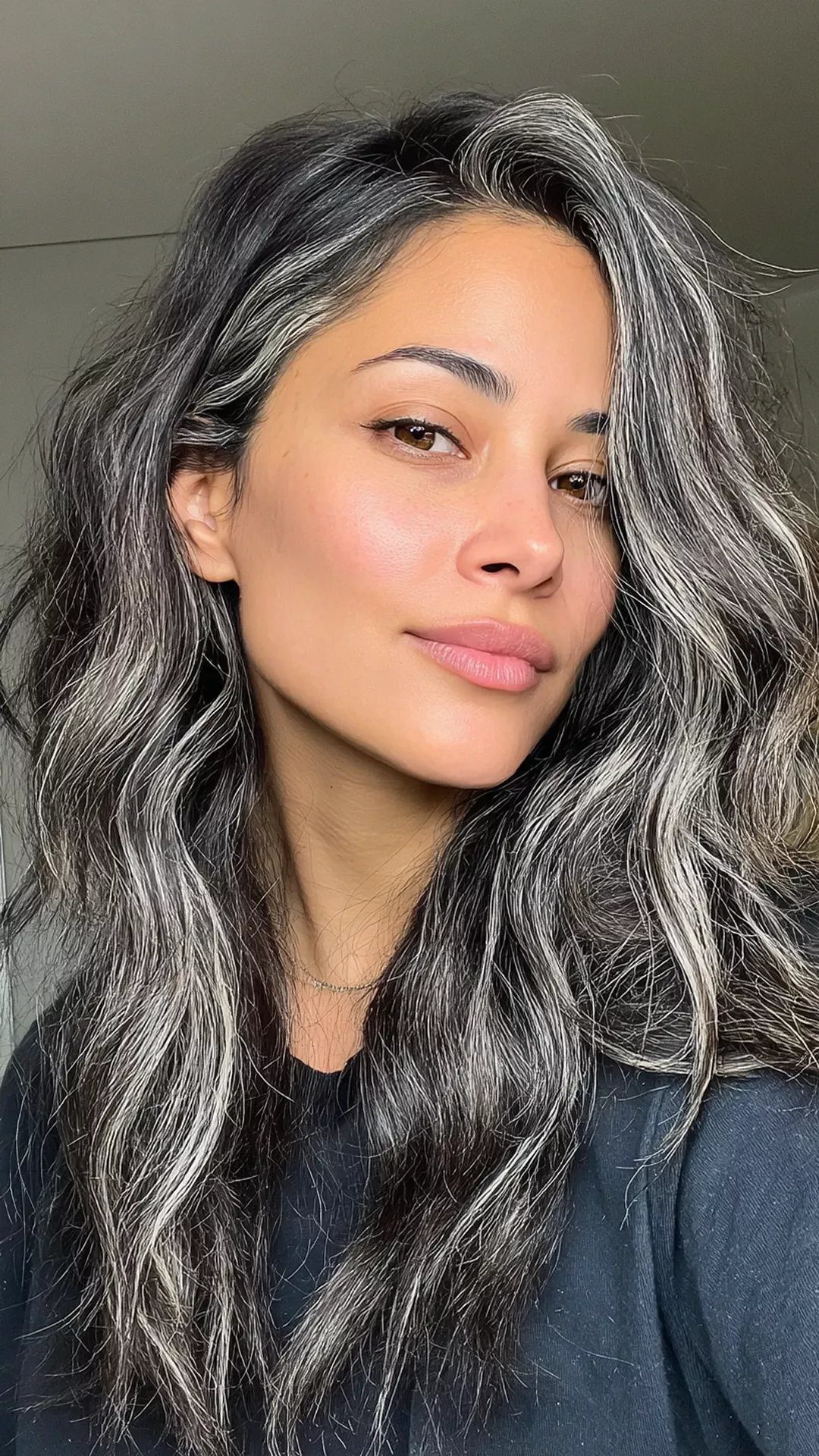 Woman with long dark hair blended with silver-gray strands at the roots and temples
