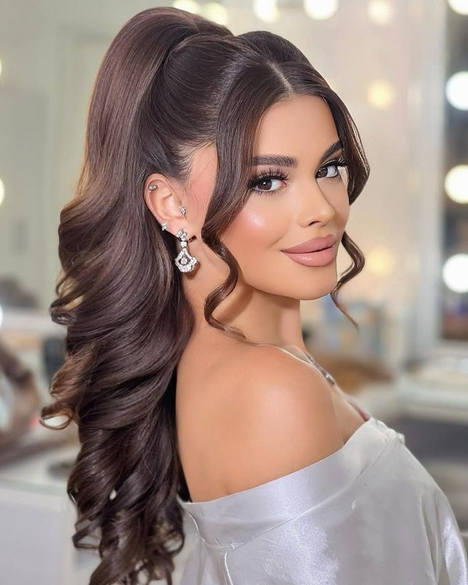 Woman wearing a high ponytail with long, glossy curls and face-framing tendrils