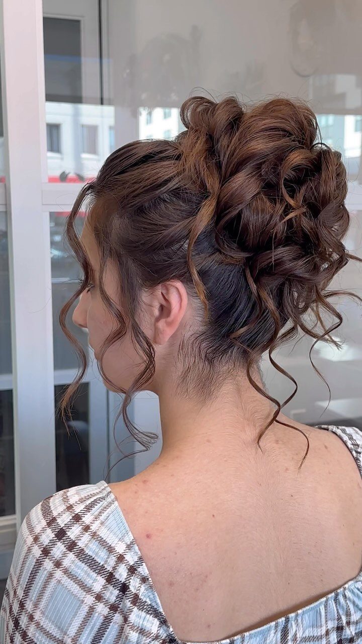 Woman wearing a voluminous brown high bun with loose curled tendrils