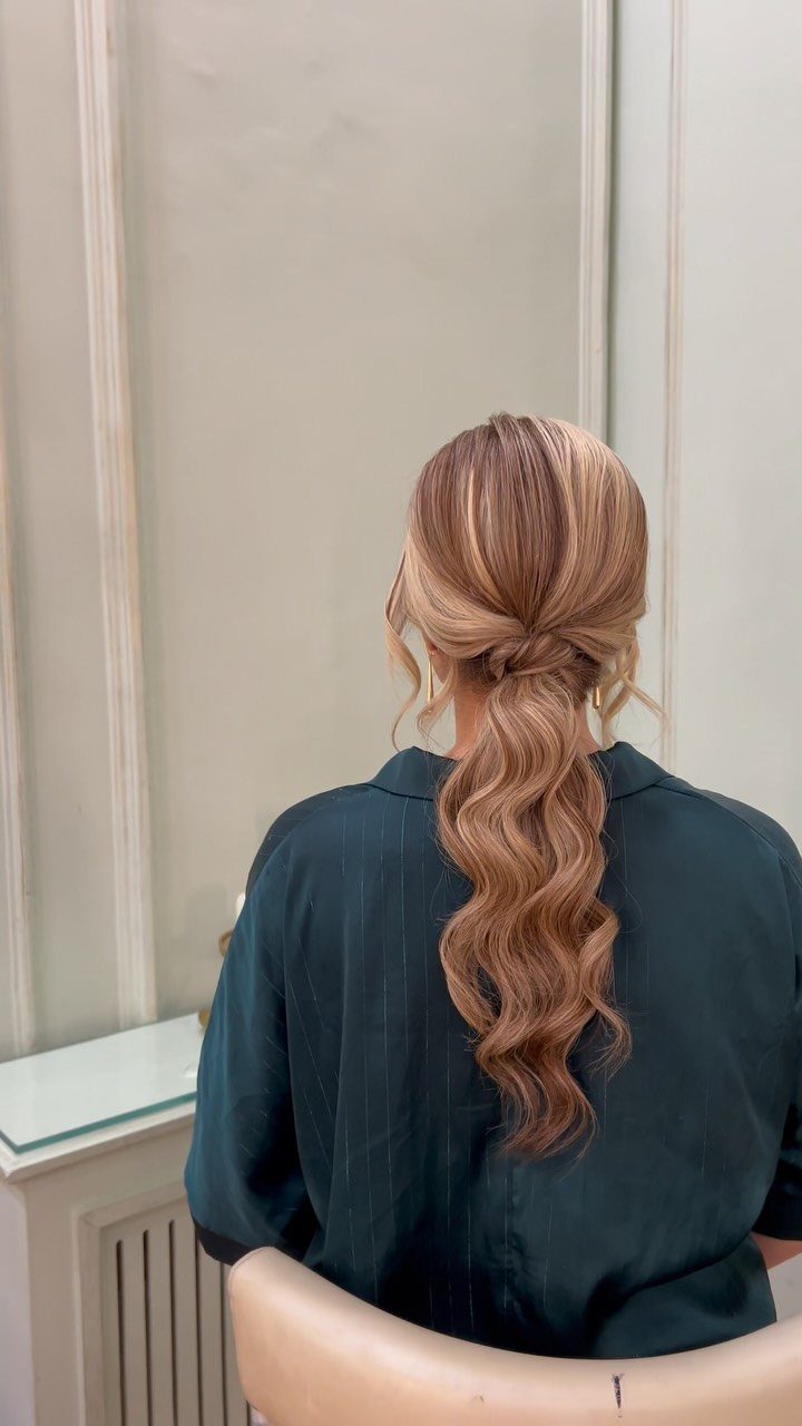 Low ponytail with a twisted base and long copper-blonde waves