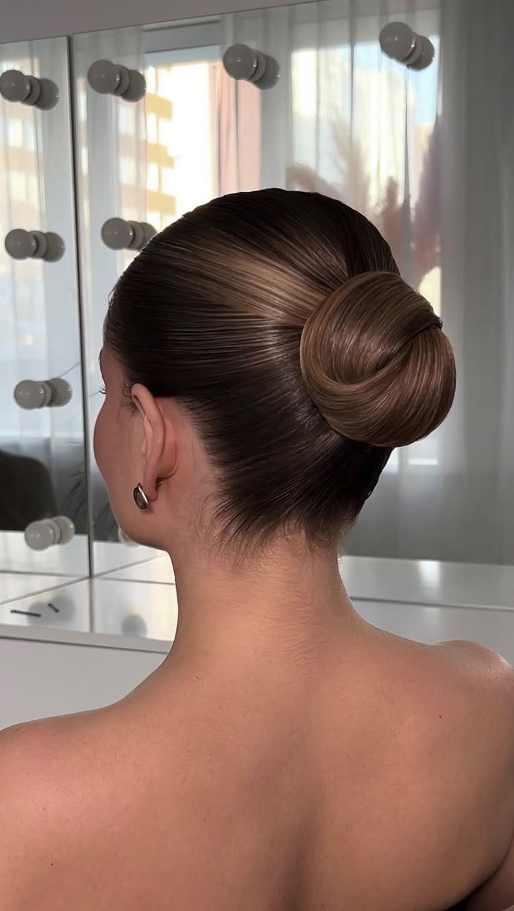 Smooth dark hair is secured in a rounded low bun at the nape