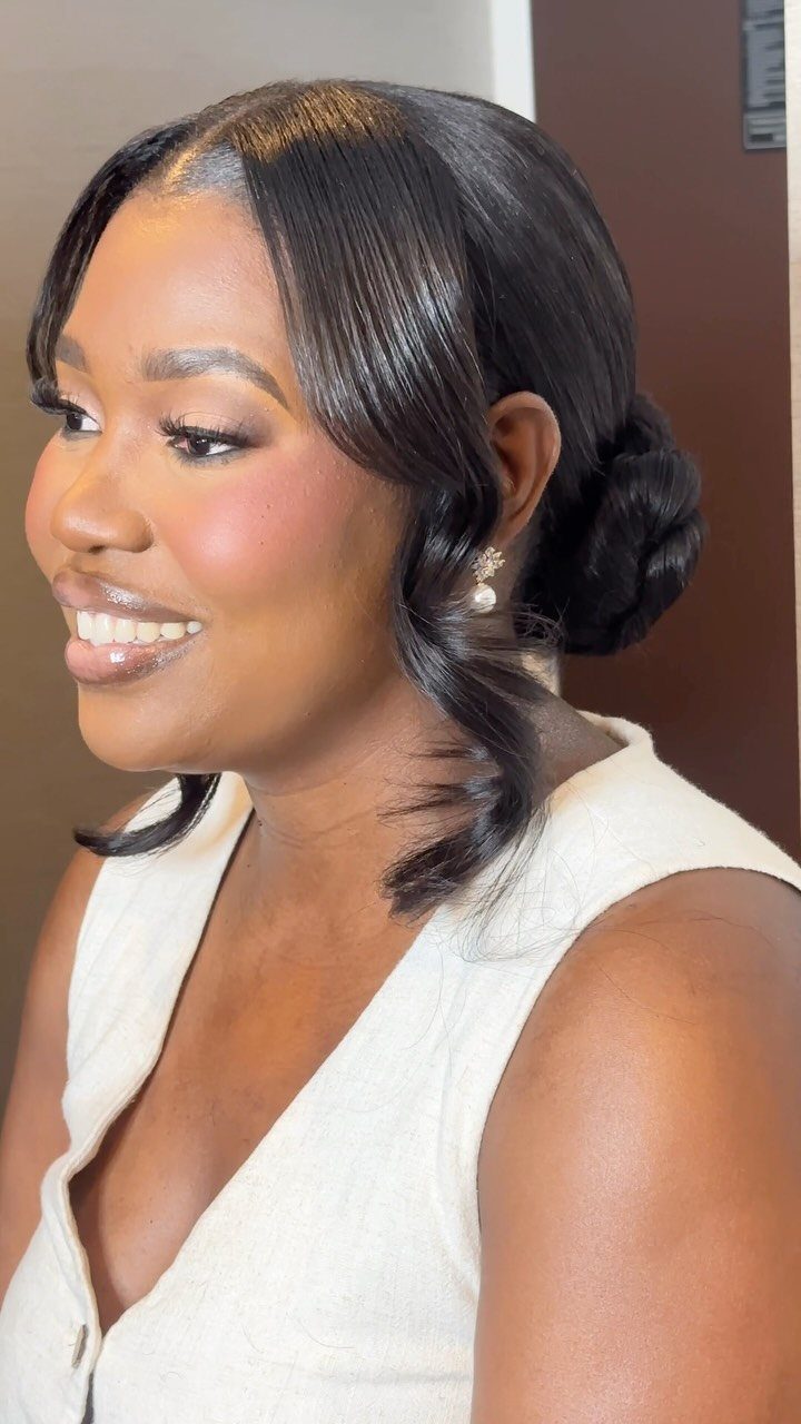 Woman wearing a sleek low twisted bun with curled face-framing tendrils