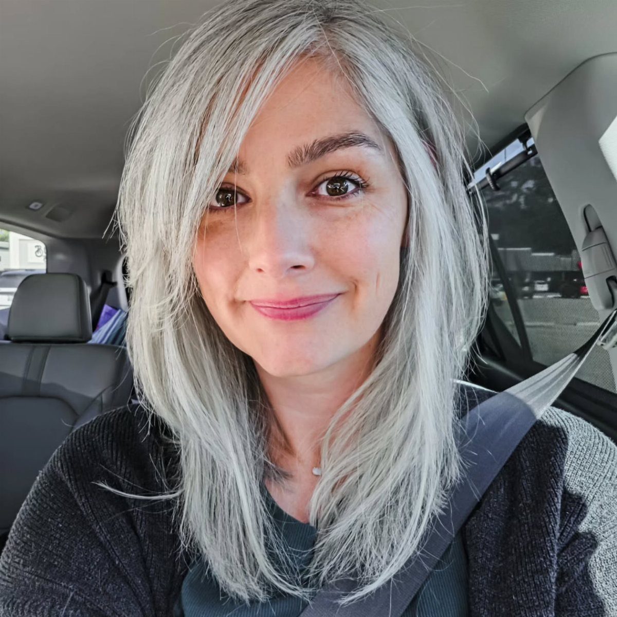 Woman showing shoulder-length silver-gray layered hair in a car selfie