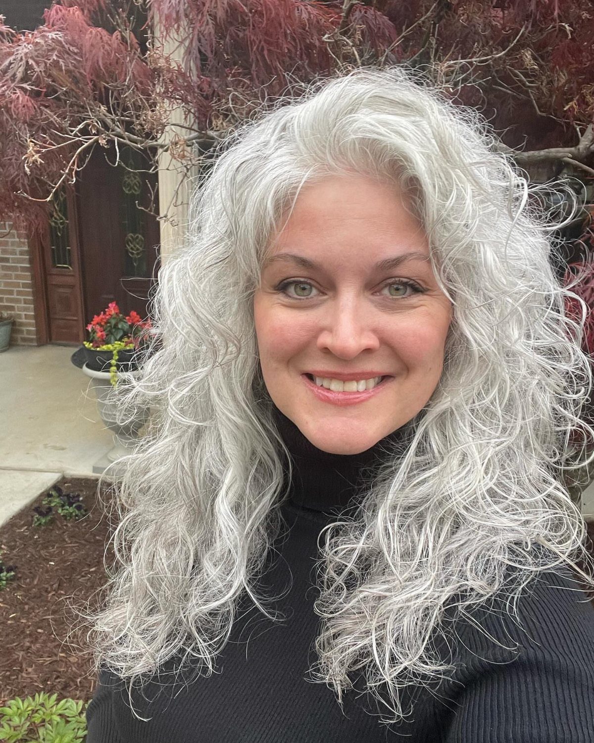 Woman with long silver-gray curls layered around her face outdoors