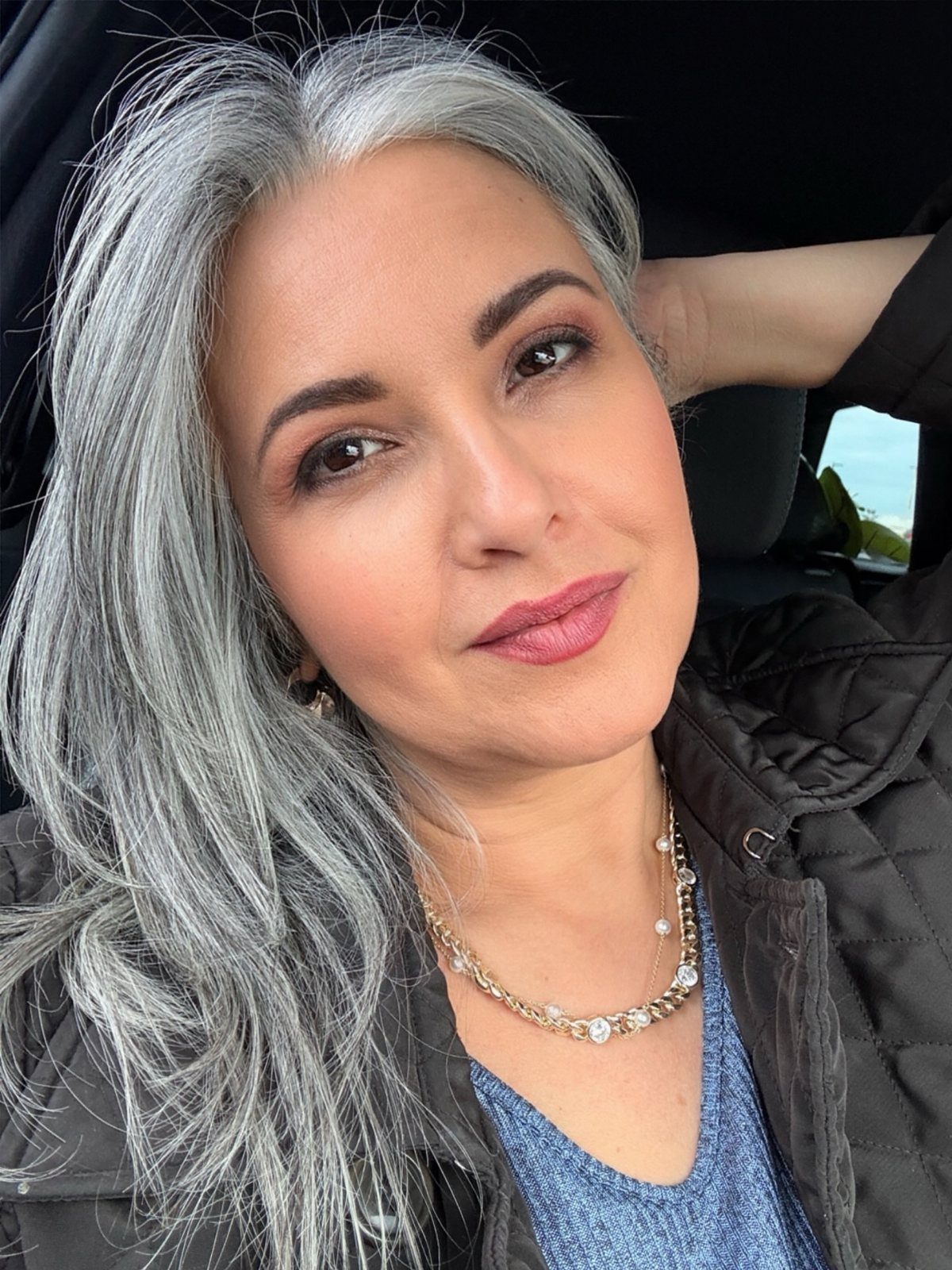 Woman poses in a car with long, straight silver-gray hair
