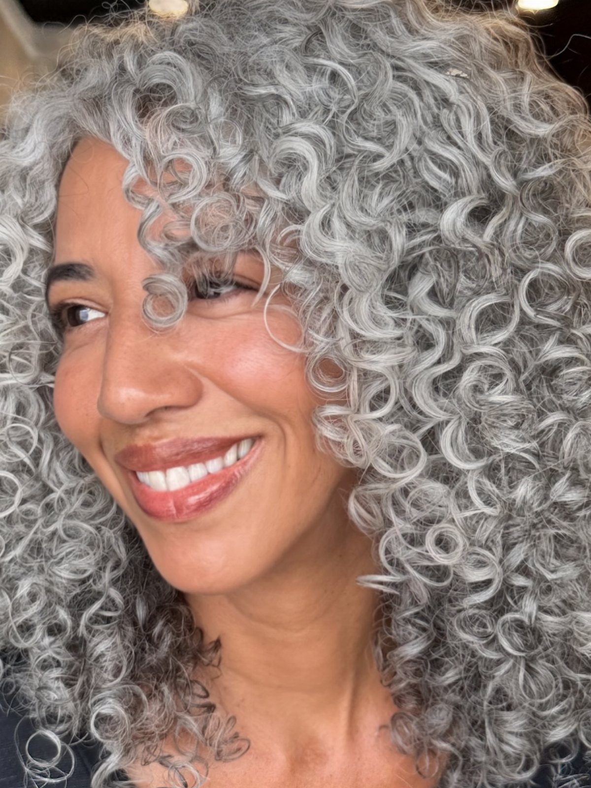 Woman smiling with long, layered silver-gray natural curls framing her face