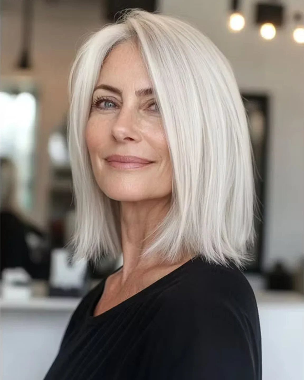 Woman posing with a sleek, straight silver-gray bob in a salon