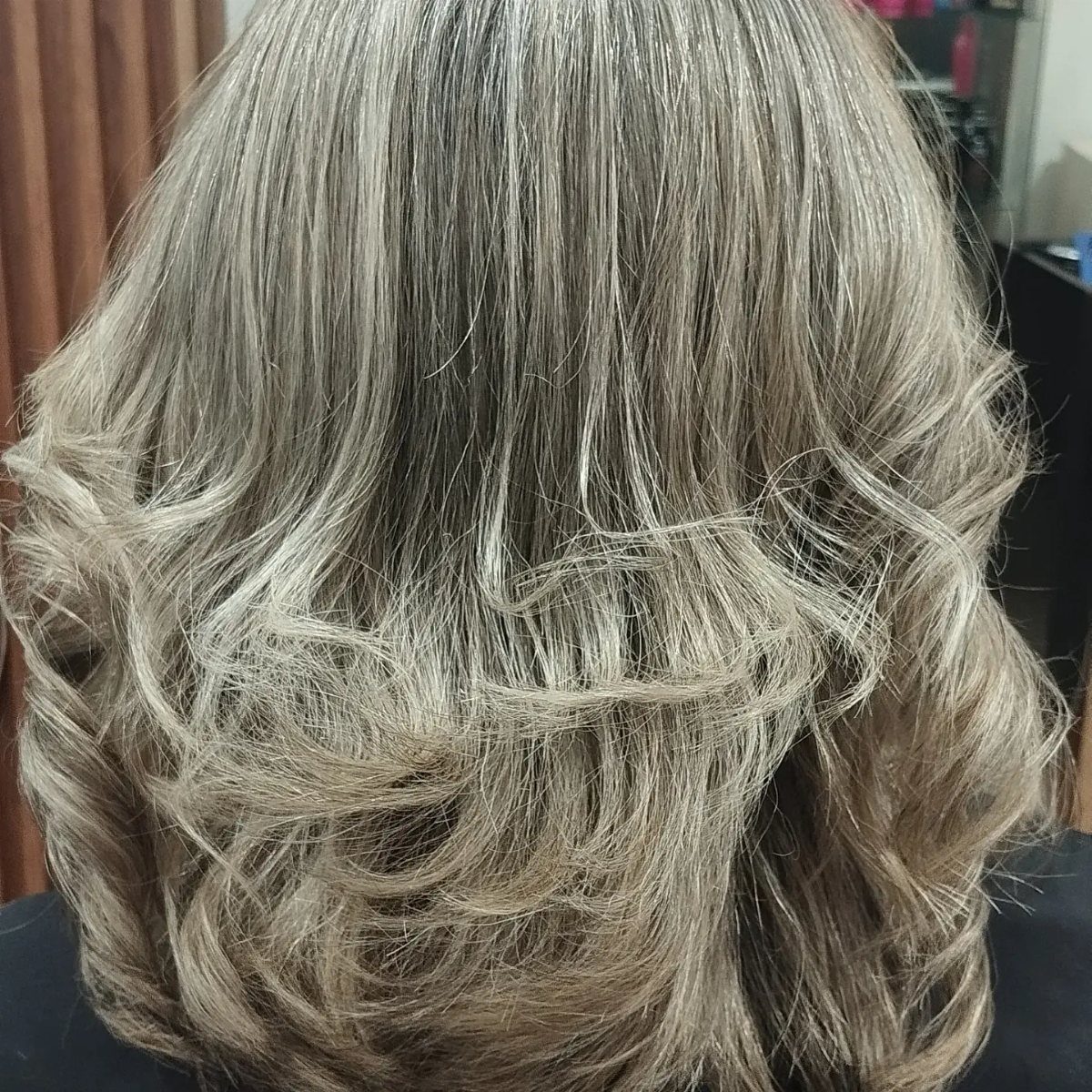 Long silver-gray hair falls in soft, layered waves against a dark salon cape
